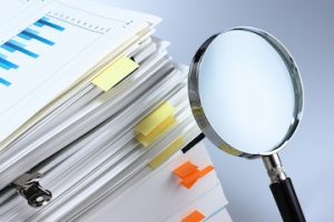Stack of documents next to a magnifying glass